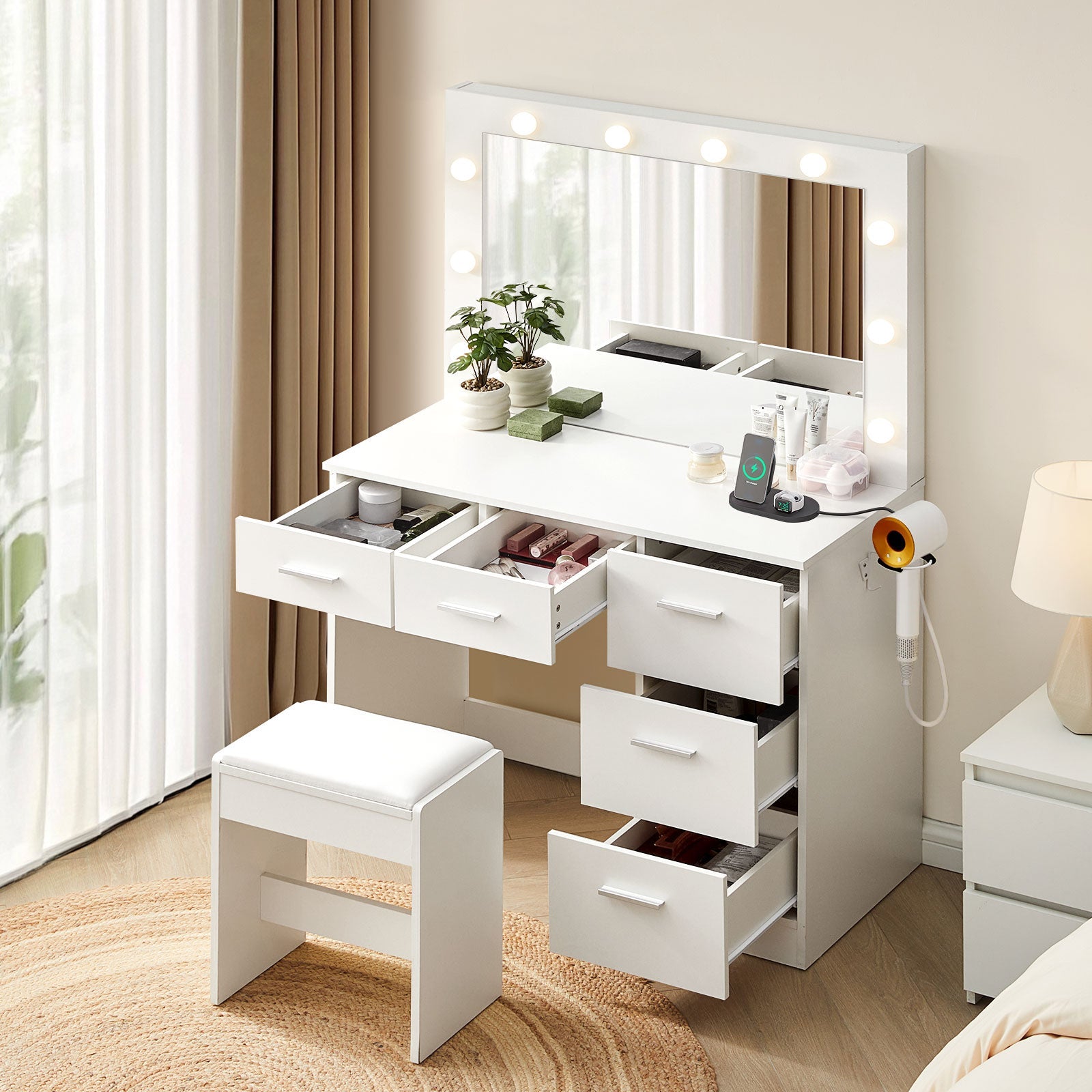 A side view of the 5-drawer Hollywood White Dressing Table with a stool, a large mirror, 10 bulbs in warm lighting mode, USB ports and power sockets, and a hairdryer holder in a bright bedroom, with all drawers open