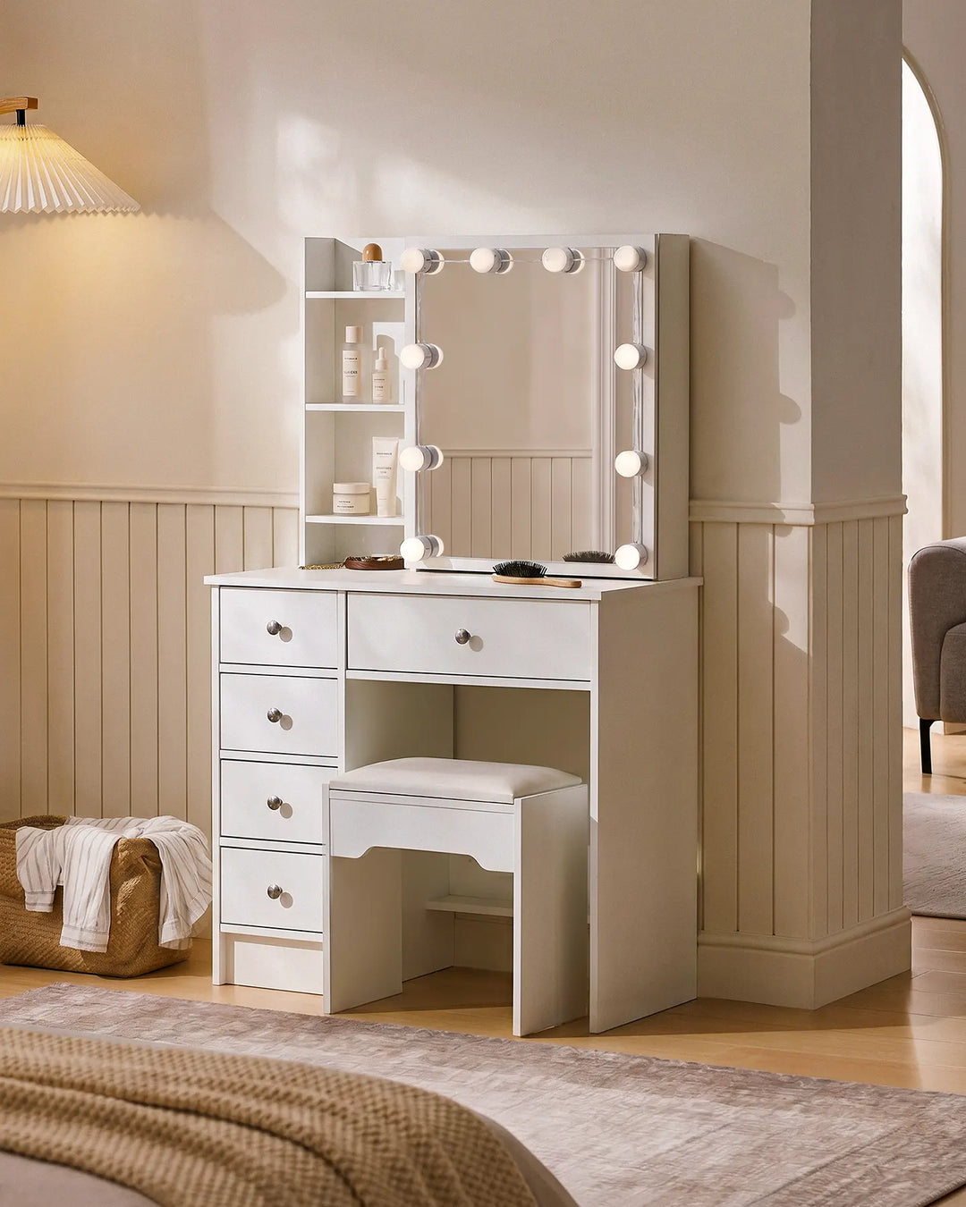 Angled view of a white dressing table with mirror, Hollywood LED bulbs, open shelving, five drawers and matching vanity stool