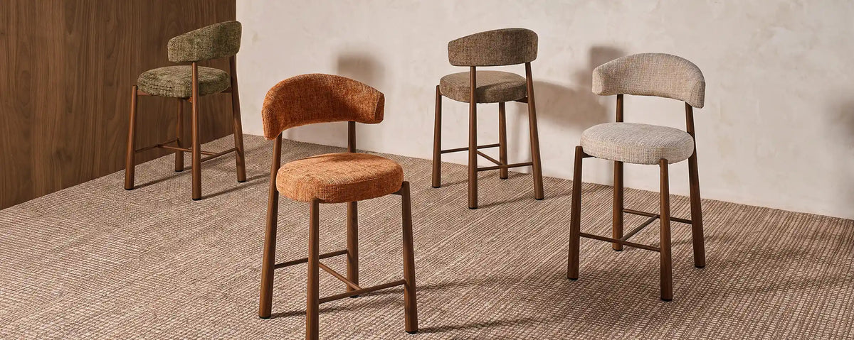 Lineup of Ansel chenille bar stools displaying available colours including oatmeal, terracotta, olive green, and Mocha brown, all with wood-effect metal legs on a woven rug