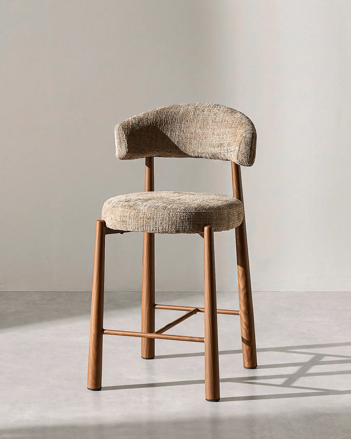 Front studio view of the Ansel bar stool highlighting the curved mocha brown chenille backrest, round cushioned seat, and wood-effect steel legs on a neutral background