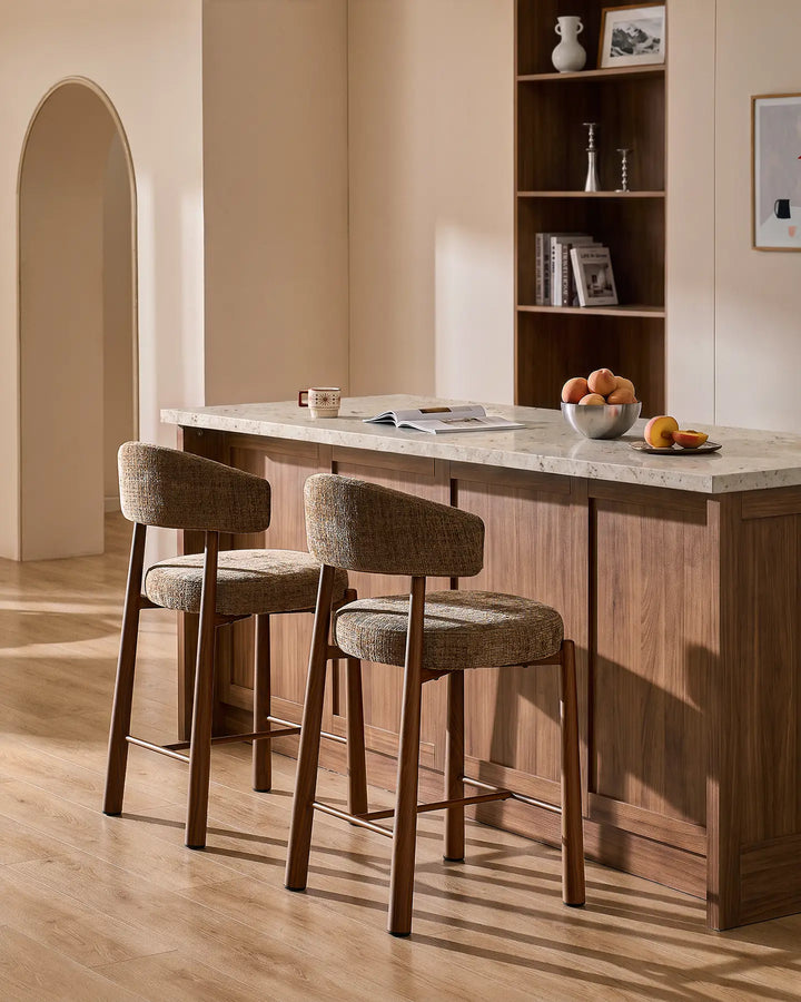 Two Ansel mocha brown chenille breakfast bar stools with wood-effect metal legs styled at a kitchen island with neutral terrazzo countertop and warm interior decor