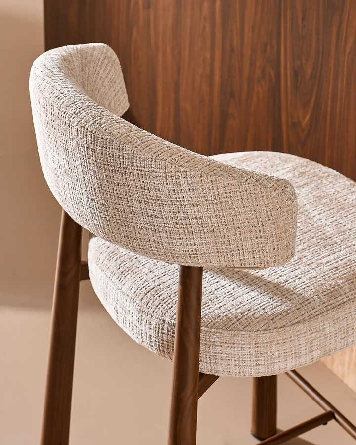 Close-up of the curved backrest cushion and wood-effect metal frame connection on the Ansel oatmeal bar stool, showing refined tailoring and durable craftsmanship