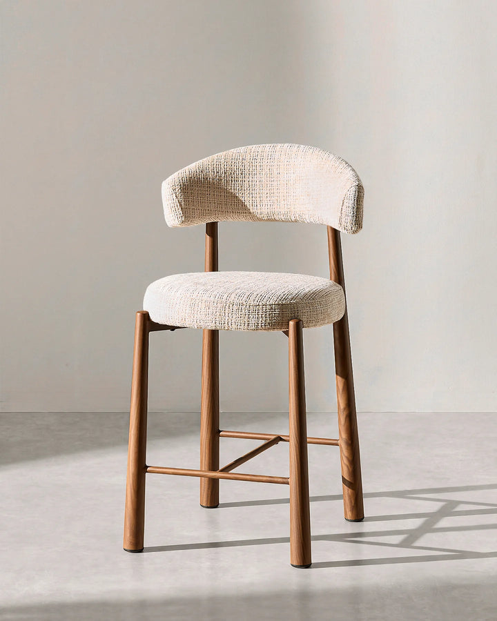 Front studio view of the Ansel bar stool highlighting the curved oatmeal chenille backrest, round cushioned seat, and wood-effect steel legs on a neutral background