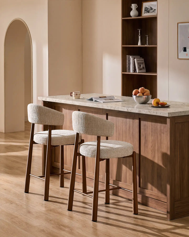 Two Ansel oatmeal chenille breakfast bar stools with wood-effect metal legs styled at a kitchen island with neutral terrazzo countertop and warm interior decor