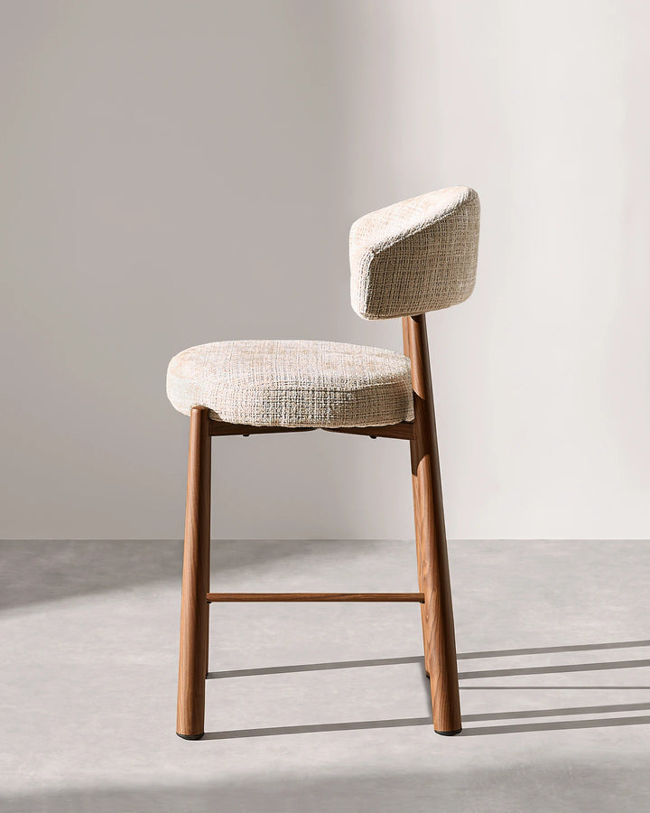 Side profile studio photograph of the Ansel oatmeal chenille bar stool showing seat depth, backrest angle, and wood-effect metal footrest height