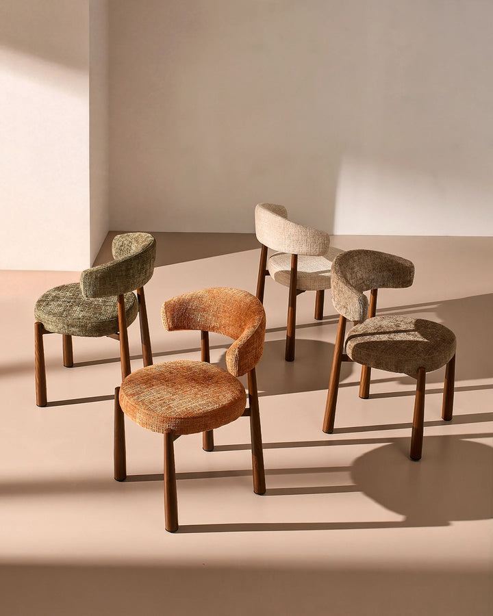 Ansel dining chairs displayed in a range of upholstery colours, including mocha and other neutral shades, with matching curved backrests and wooden-effect legs.