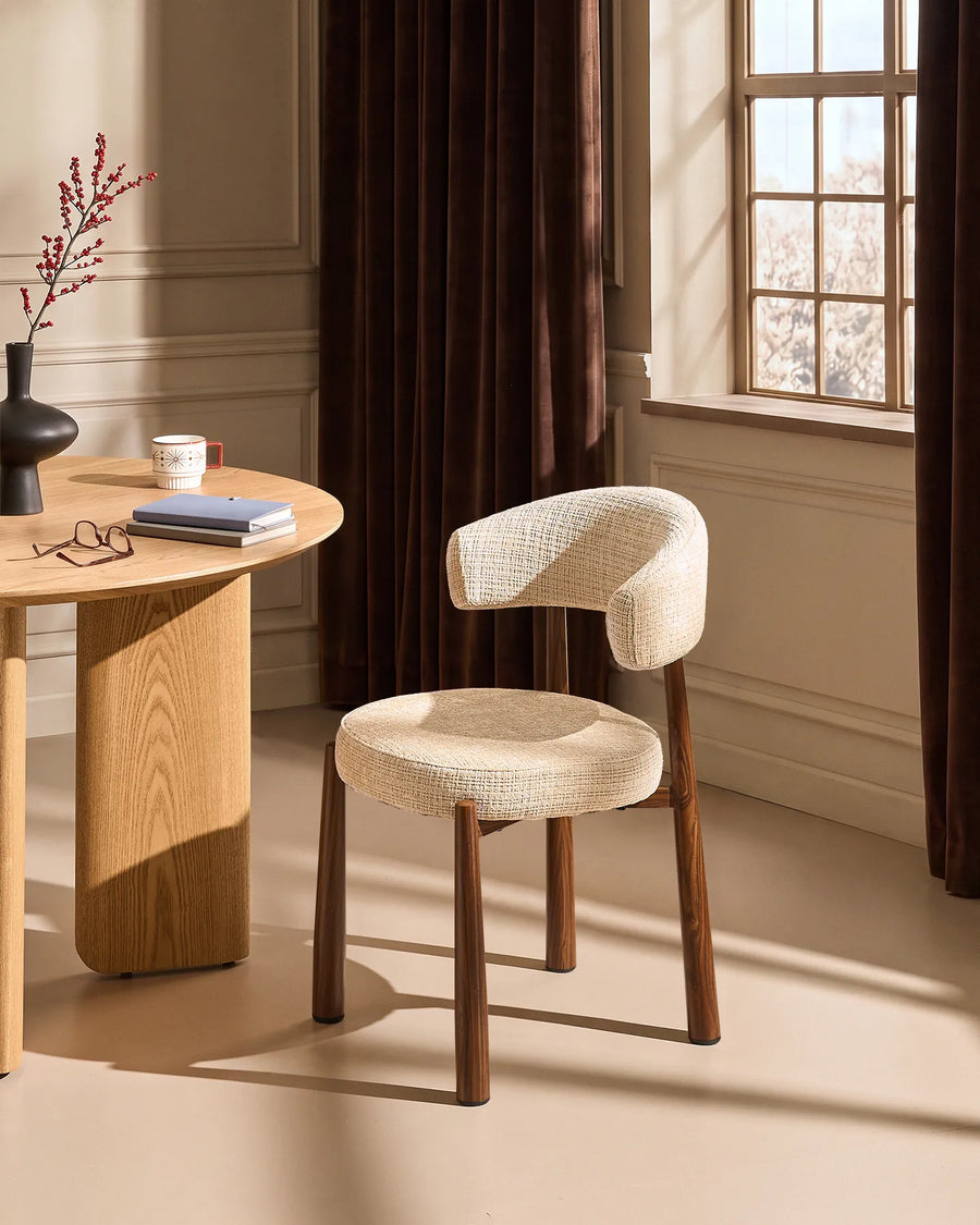 Ansel Oatmeal Chenille Dining Chair with curved upholstered backrest and wooden-effect legs beside a light oak dining table in a warm neutral dining room.