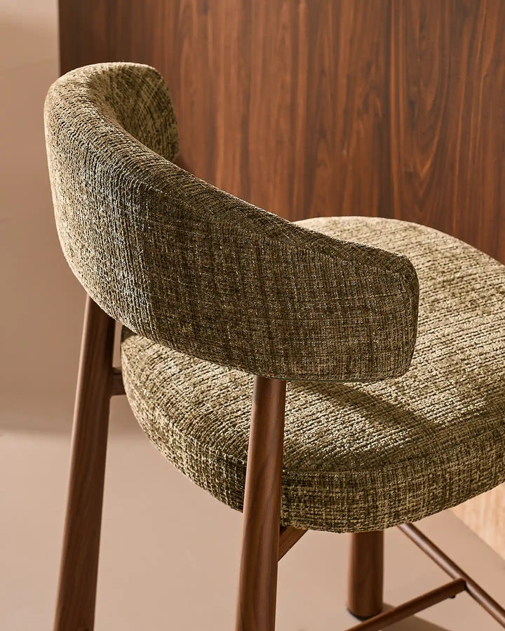 Close-up of the curved backrest cushion and wood-effect metal frame connection on the Ansel olive green bar stool, showing refined tailoring and durable craftsmanship