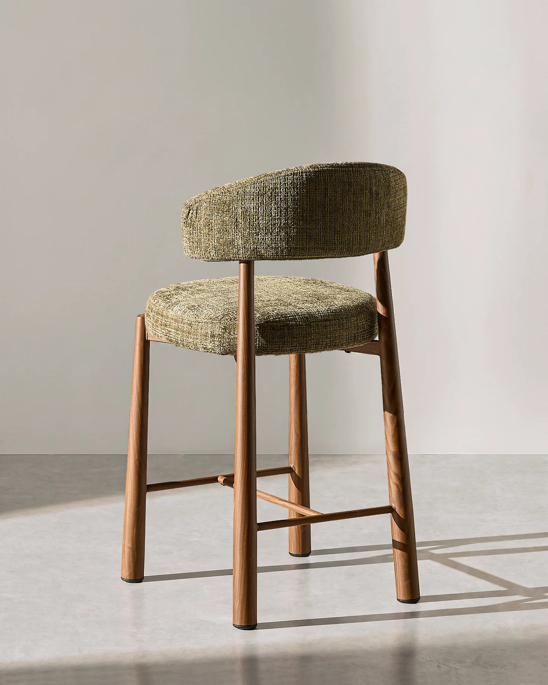 Rear three-quarter studio view of the Ansel olive green chenille bar stool displaying the curved ergonomic backrest and durable wood-effect metal frame structure