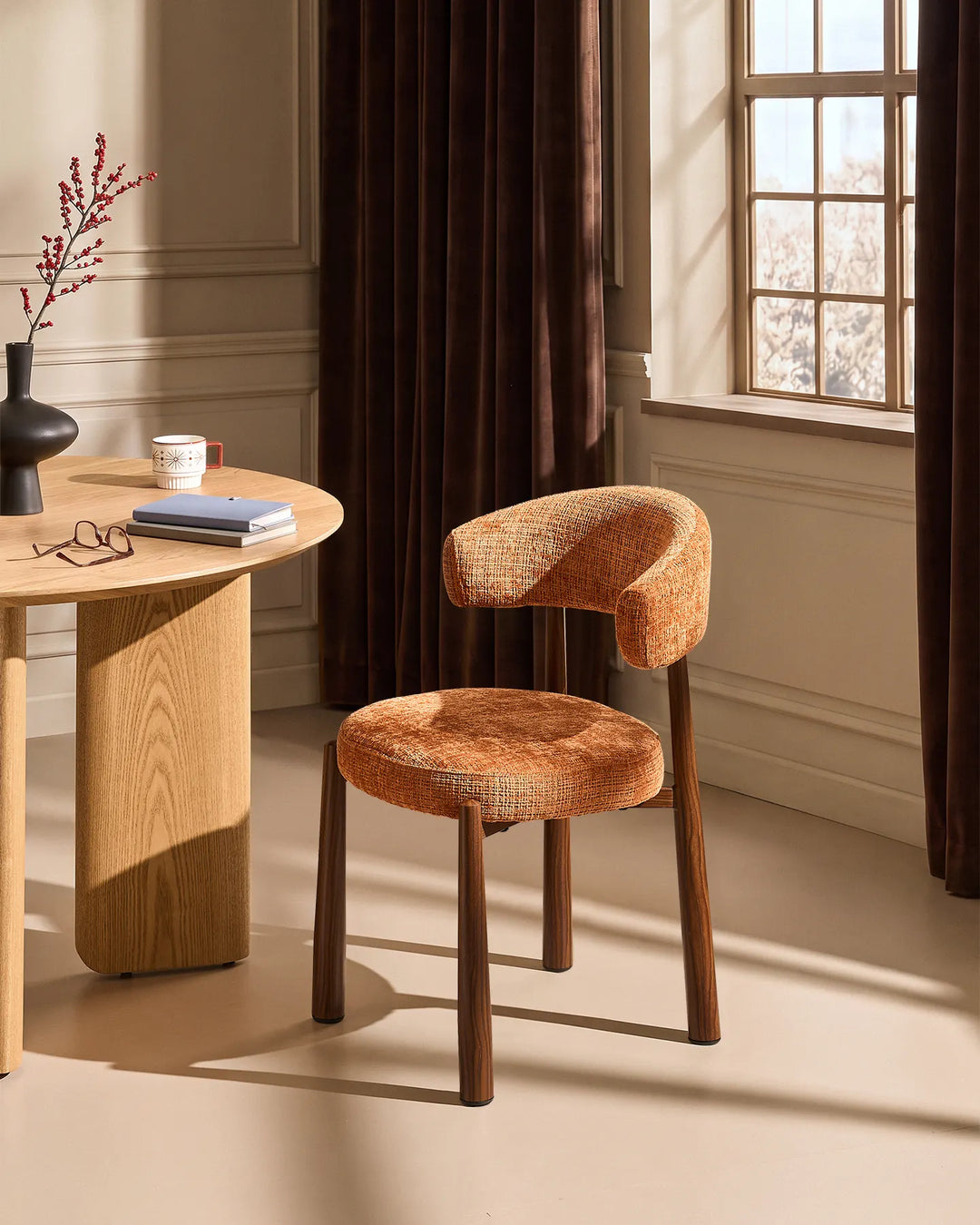 Ansel Terracotta Chenille Dining Chair with curved upholstered backrest and wooden-effect legs beside a light oak dining table in a warm neutral dining room.