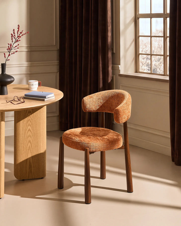 Ansel Terracotta Chenille Dining Chair with curved upholstered backrest and wooden-effect legs beside a light oak dining table in a warm neutral dining room.