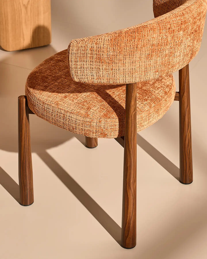 Close-up of the Ansel Terracotta Chenille Dining Chair showing its textured upholstery, curved backrest and tapered wooden-effect legs.
