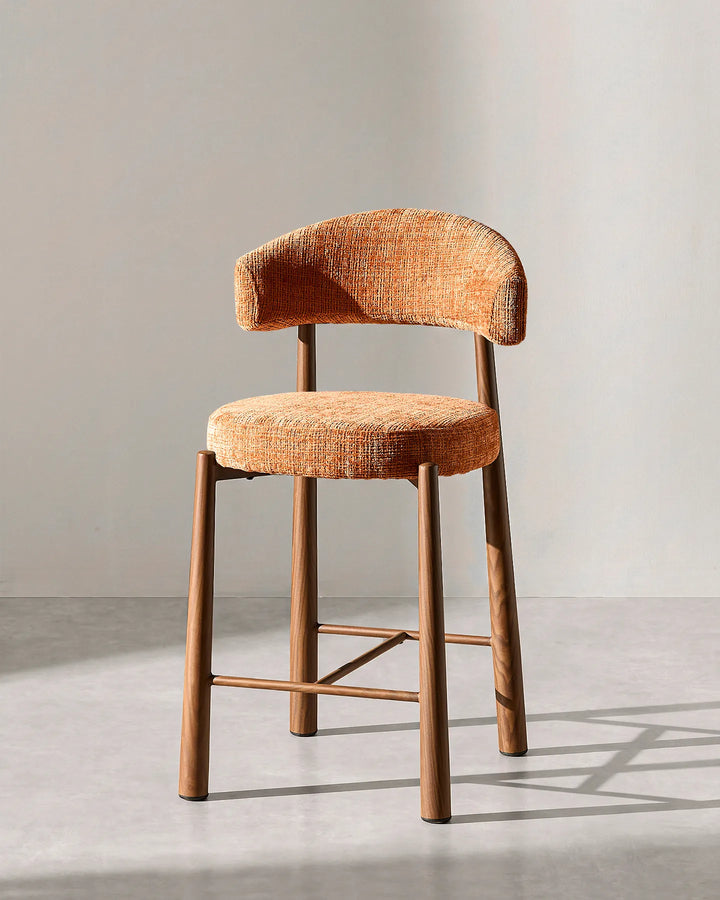 Front studio view of the Ansel bar stool highlighting the curved terracotta orange chenille backrest, round cushioned seat, and wood-effect steel legs on a neutral background