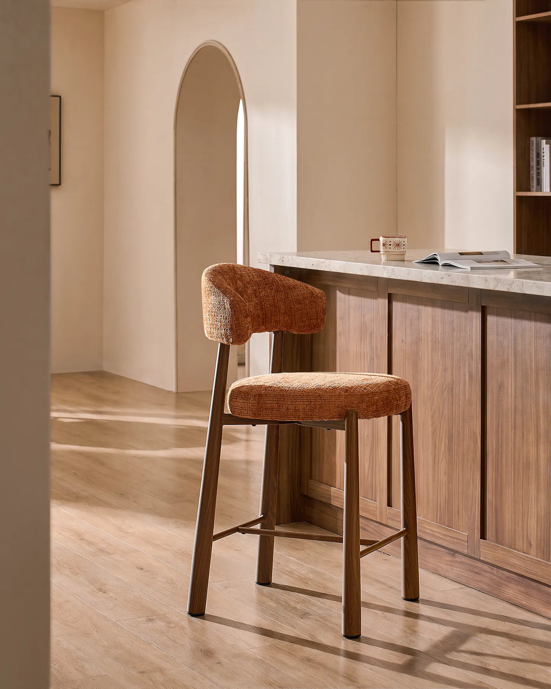 Ansel bar stool in terracotta orange textured chenille fabric with wood-effect metal legs positioned beside a modern kitchen island with stone worktop in a warm minimalist home