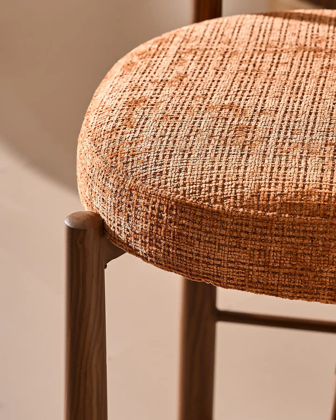 Macro detail of the rounded seat cushion corner on the Ansel bar stool, highlighting the textured terracotta orange chenille weave and wood-effect steel leg joint