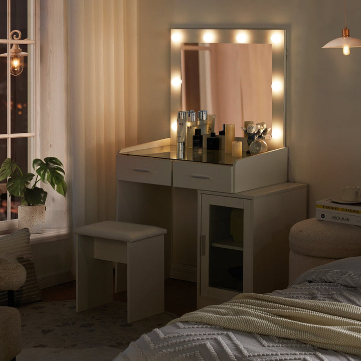 The side view of the white dressing table set, featuring a glass tabletop, a mirror, 8 bright bulbs, 2 drawers, a cabinet with a glass door, and a stool,  in a bedroom, at night.
