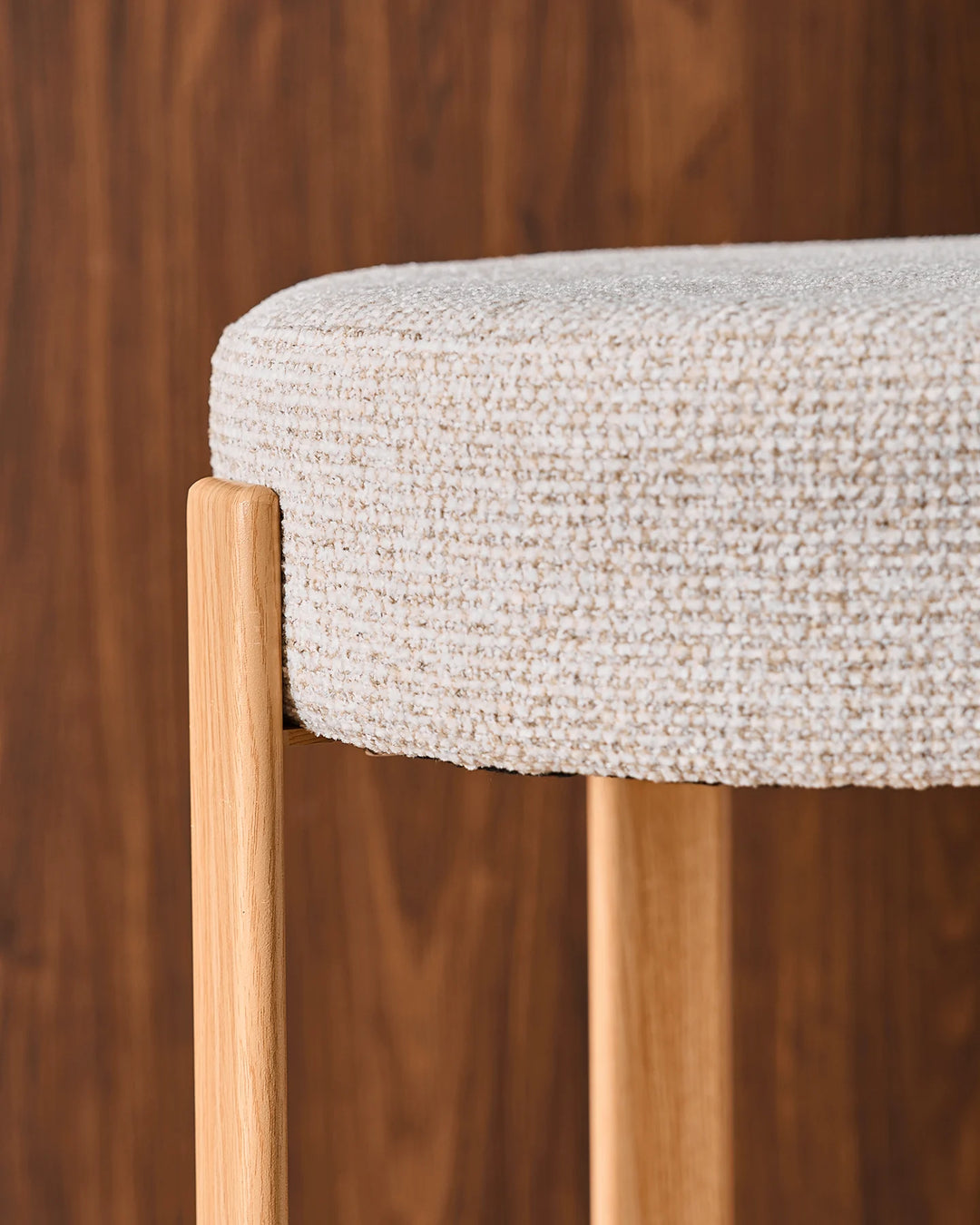 Close-up of a Bramley cream chenille bar stool showing the wood-effect veneer frame, slim legs and curved circular footrest