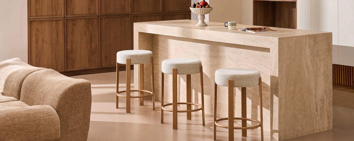 Bramley cream chenille backless bar stools arranged around a kitchen island in a warm contemporary interior, showcasing their compact backless design