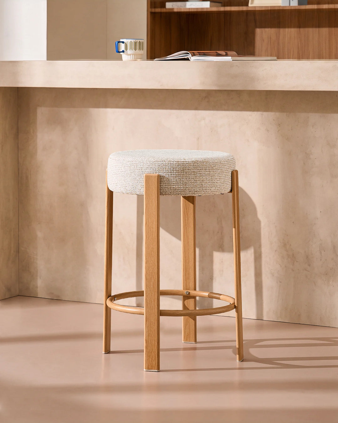 Bramley cream chenille backless bar stool placed at a modern kitchen island, combining textured upholstery with a warm wood-effect veneer finish