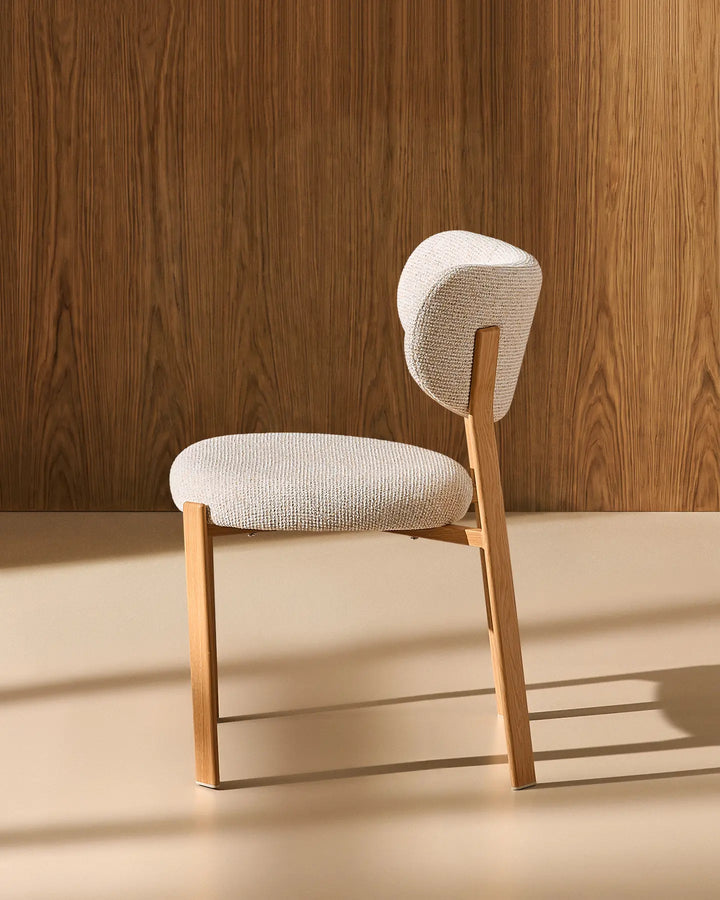 Angled view of the Bramley cream chenille dining chair, showing its curved upholstered seat and backrest with slender wood-effect legs