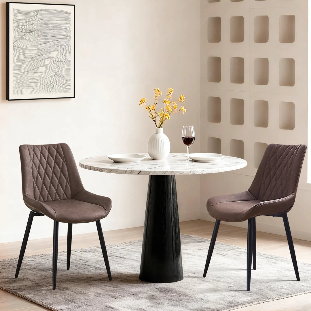 Carl Dining Chair - displaying a set of 2 brown chairs around a round dining table on a grey carpet, there are plates and a vase on the table, and a wall picture on the white wall.