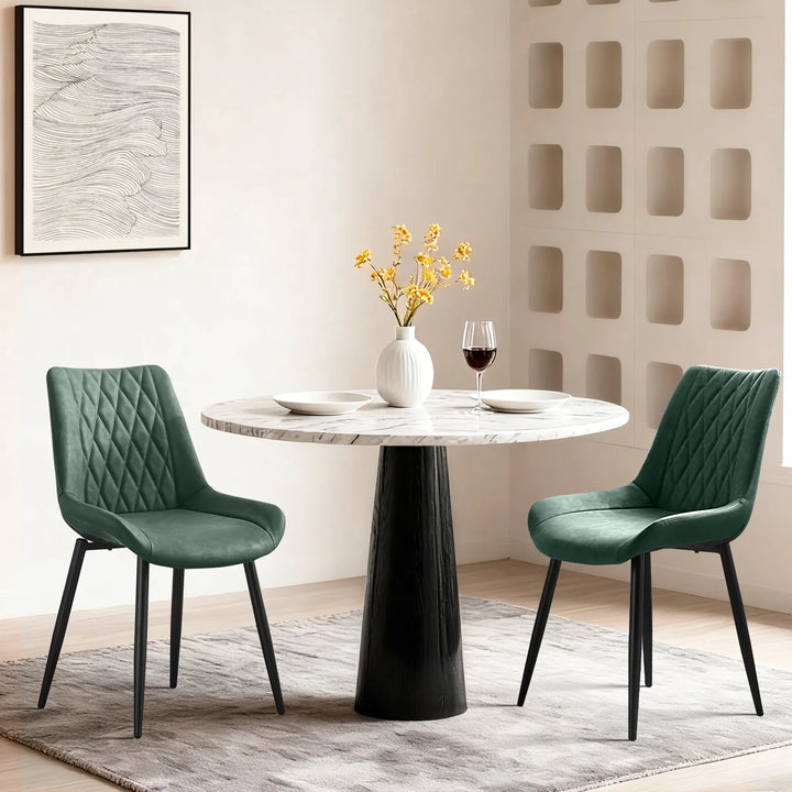 Carl Dining Chair - displaying a set of 2 green chairs around a round dining table on a grey carpet, there are plates and a vase on the table, and a wall picture on the white wall. 