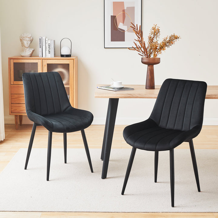 Set of 2 black velvet dining chairs with black metal legs, placed by a wooden dining table in a modern dining room setting