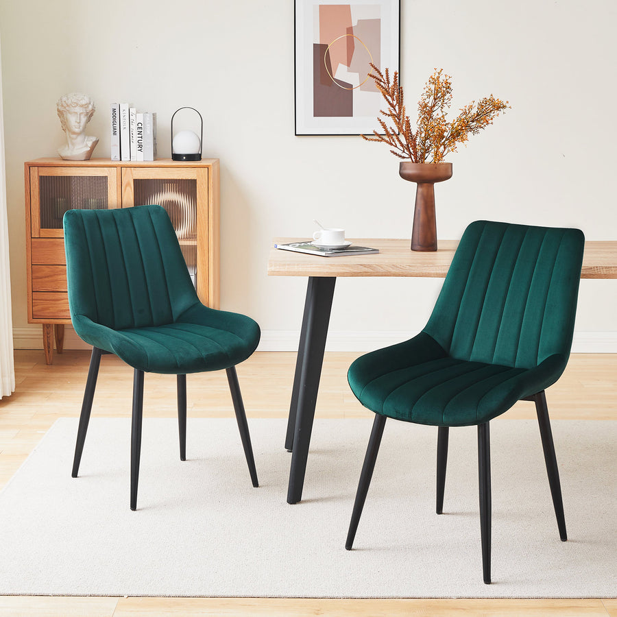Set of 2 green velvet dining chairs with black metal legs, placed by a wooden dining table in a modern dining room setting