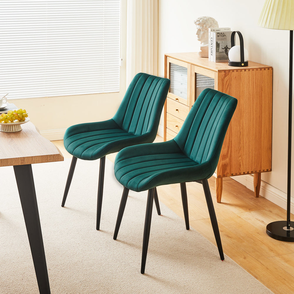 Set of 2 green velvet dining chairs with black metal legs placed on the same side of a wooden dining table in a modern dining room
