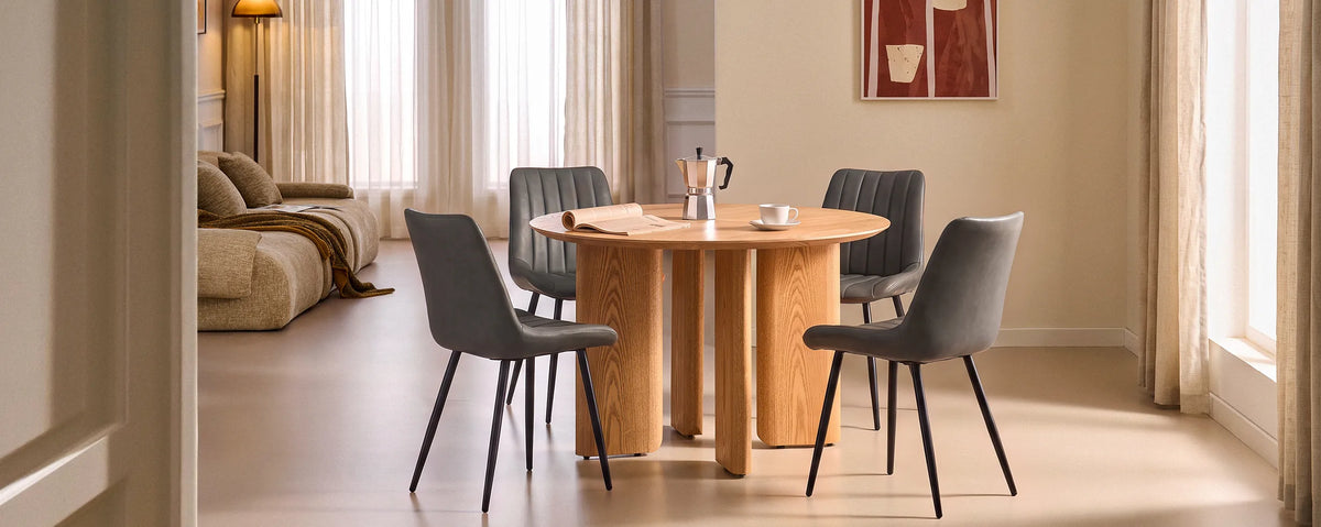 Wide panoramic view of a set of 4 Clair grey faux leather dining chairs arranged around a stylish round dining table in an open-plan living and dining area.