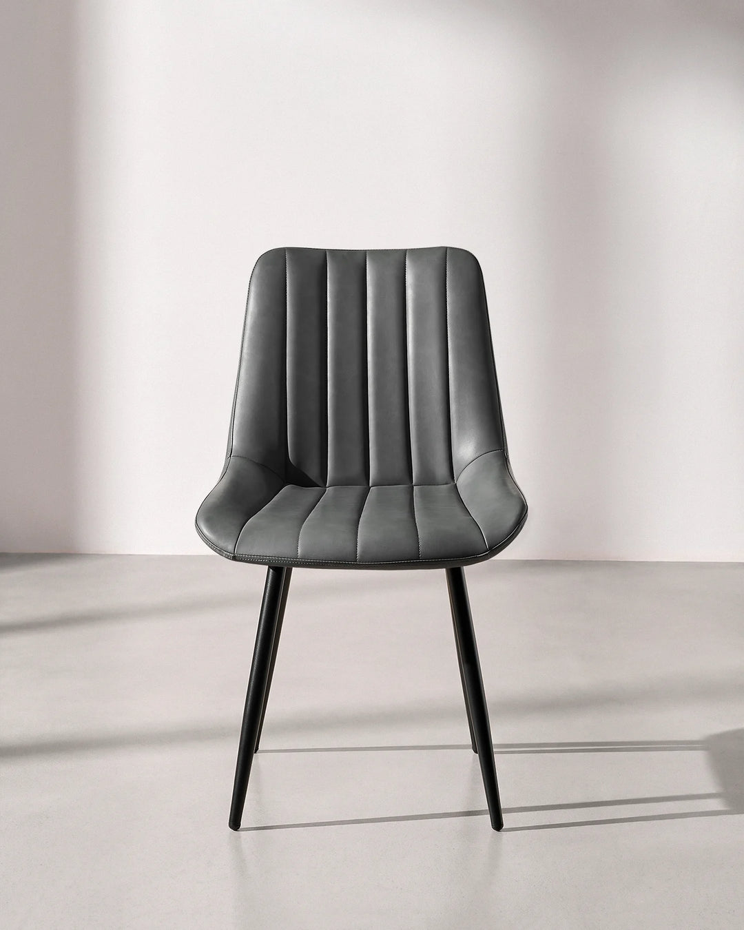Front view of the Clair grey faux leather dining chair, highlighting the fluted vertical ribbed backrest and durable black metal frame.