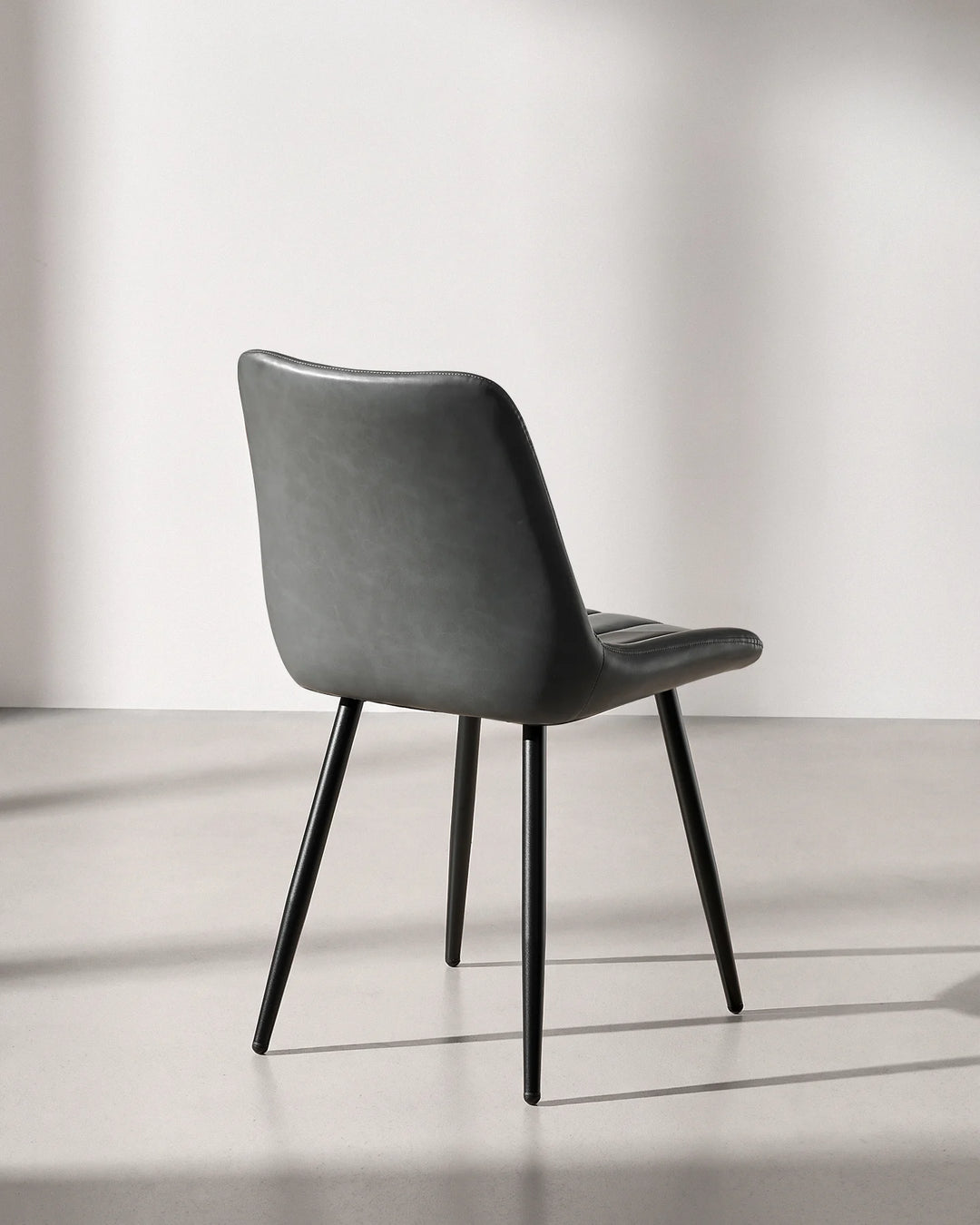 Rear three-quarter view of the Clair grey faux leather dining chair, showing smooth wipe-clean upholstery on the back and sturdy steel legs.