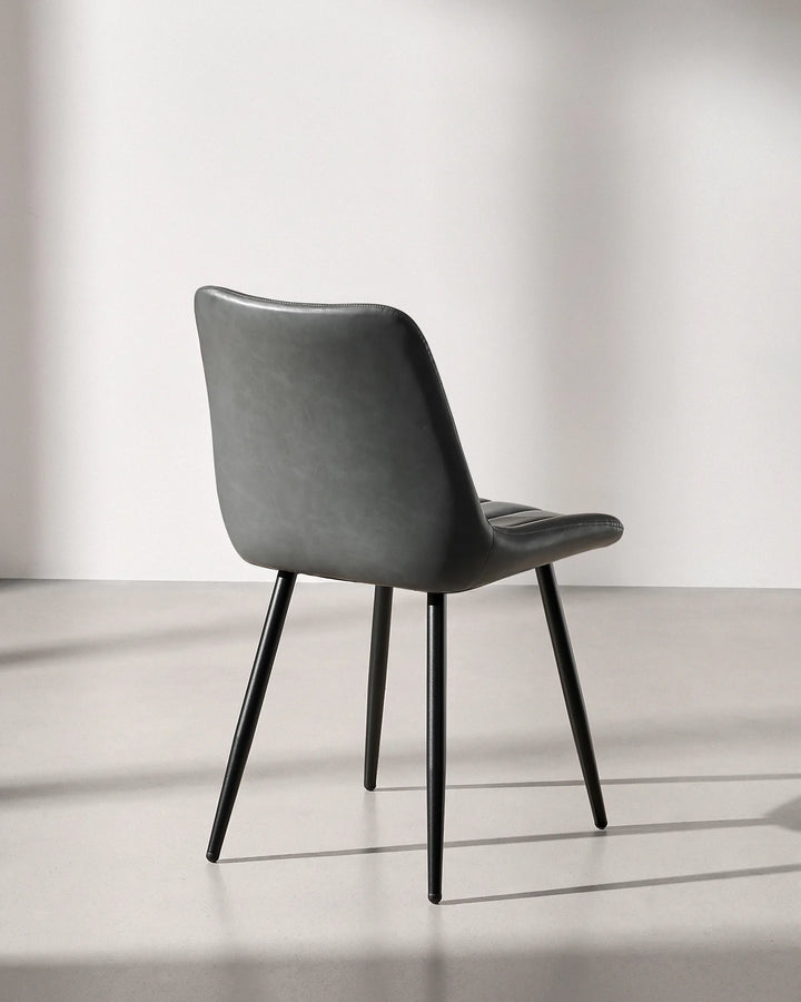 Rear three-quarter view of the Clair grey faux leather dining chair, showing smooth wipe-clean upholstery on the back and sturdy steel legs.