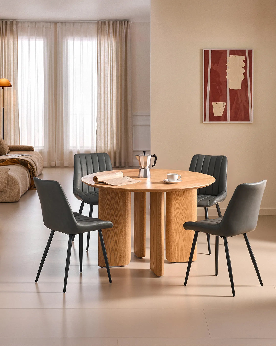 Set of 4 Clair grey faux leather dining chairs with sleek black tapered legs surrounding a round wooden dining table in a bright modern British home.