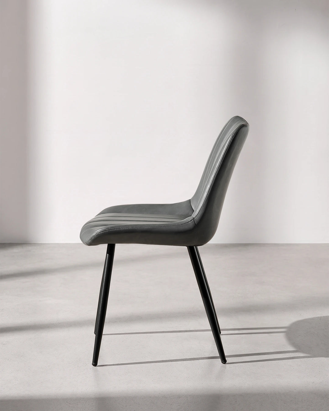 Side profile view of the Clair grey faux leather dining chair, displaying the ergonomic curved lumbar back support and slimline silhouette.