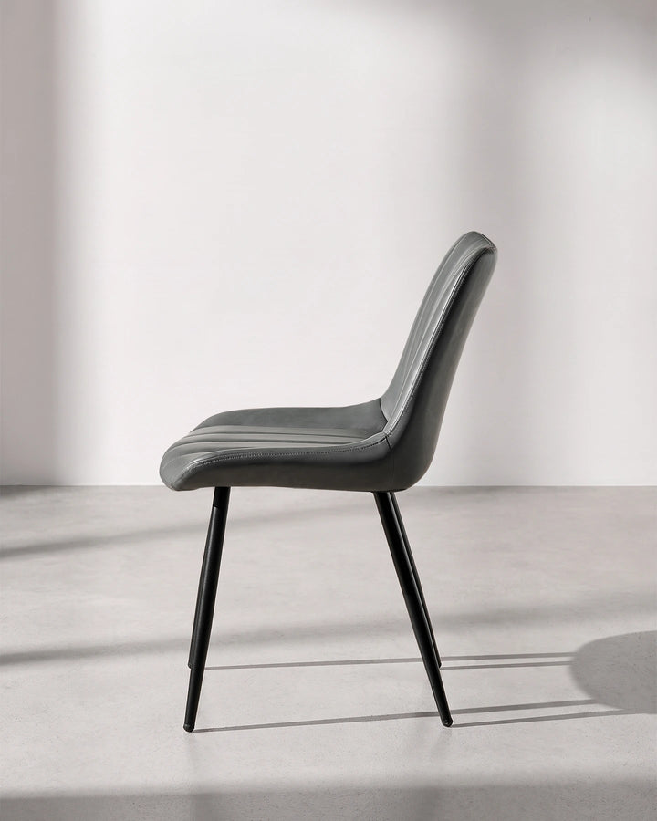 Side profile view of the Clair grey faux leather dining chair, displaying the ergonomic curved lumbar back support and slimline silhouette.