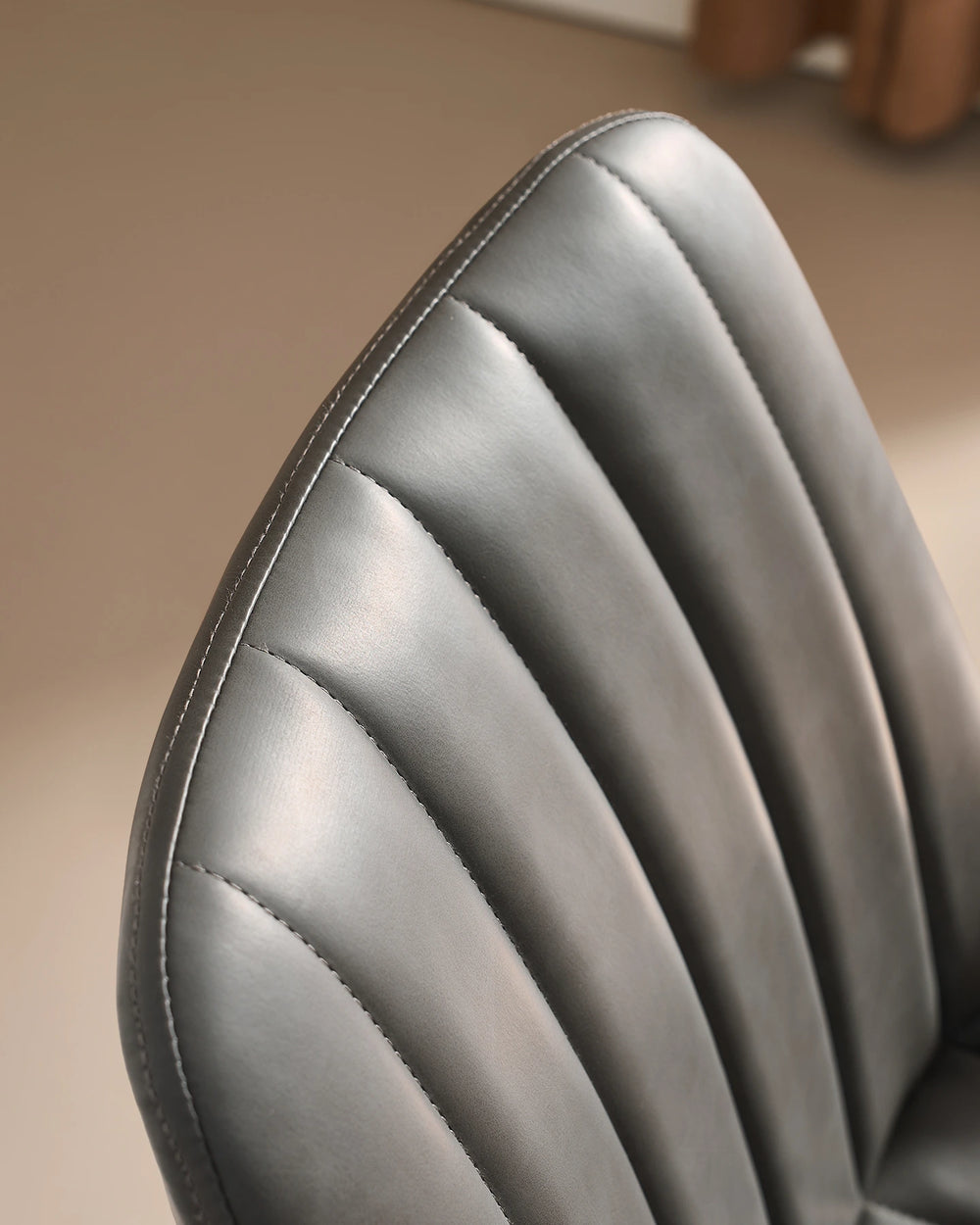 Close-up detail of the neat stitched seam and fluted ribbed cushioning along the top curved edge of the Clair grey faux leather dining chair.