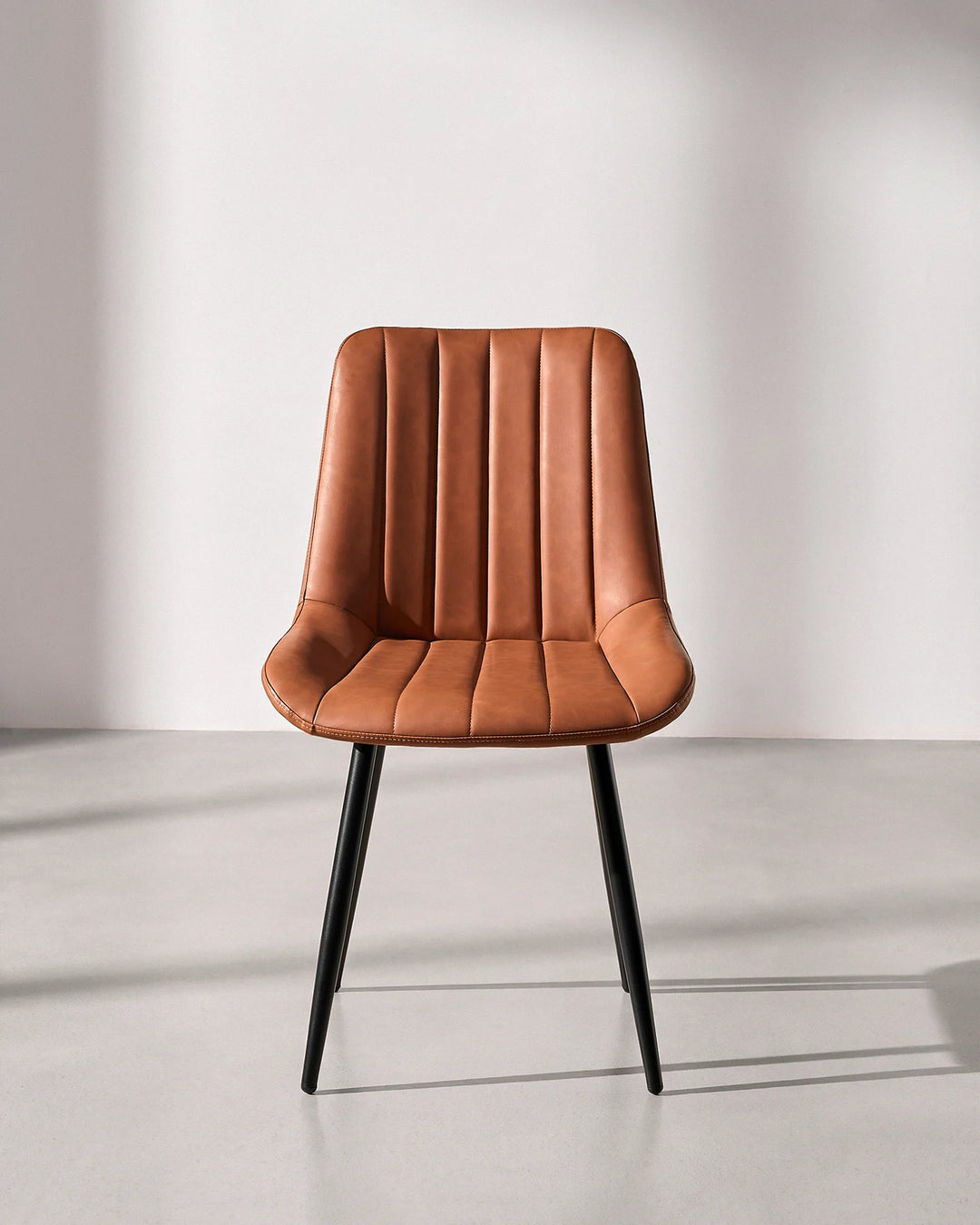 Front view of the Clair tan brown faux leather dining chair, highlighting the fluted vertical ribbed backrest and durable black metal frame.