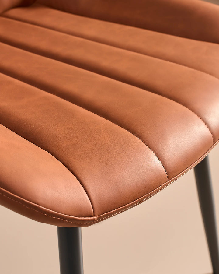 High-angle close-up of the thick padded foam seat cushion on the Clair tan brown faux leather dining chair, engineered for everyday dining comfort.