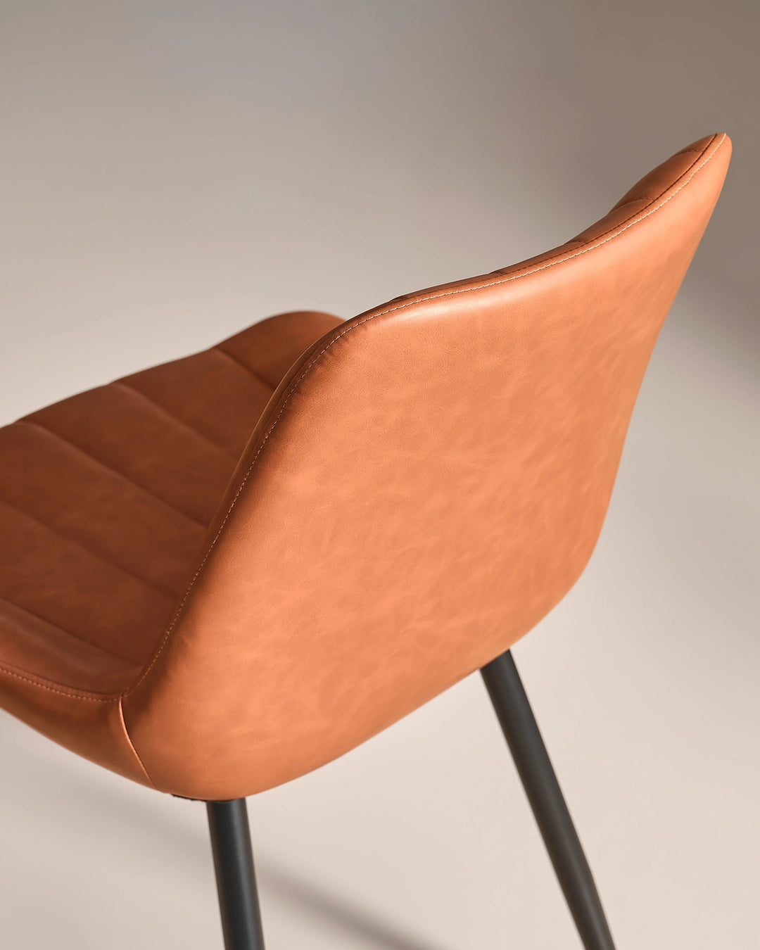 Detailed close-up showing the smooth tan brown faux leather finish on the reverse of the backrest and the black powder-coated metal leg fixture.