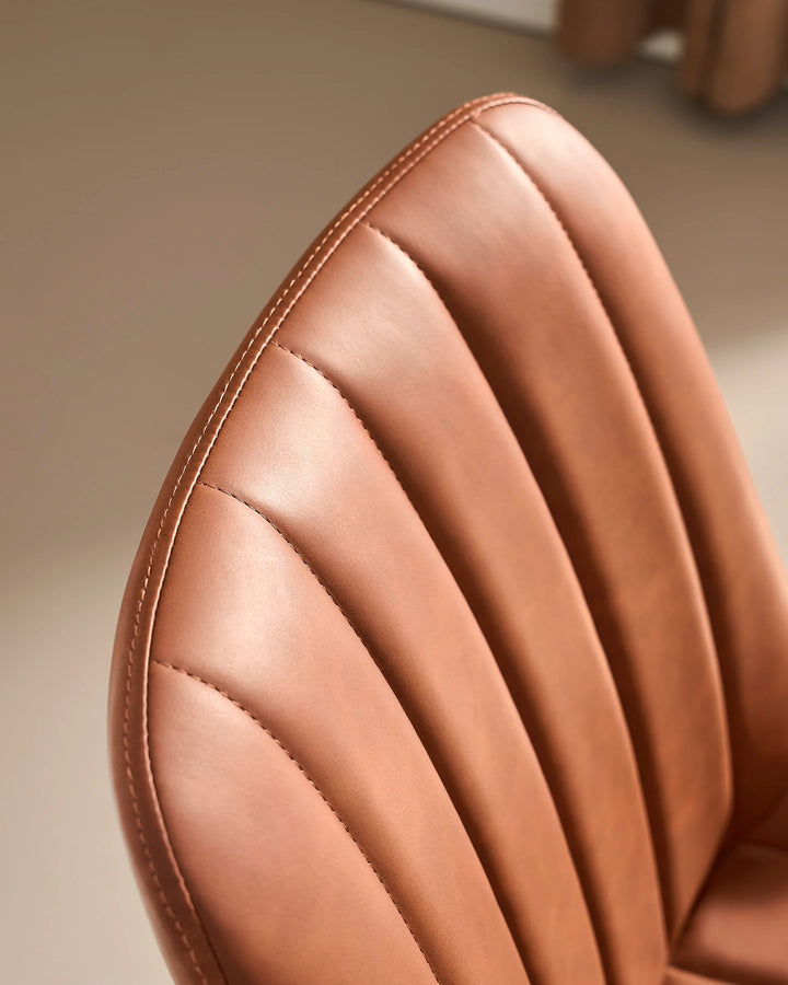 Close-up detail of the neat stitched seam and fluted ribbed cushioning along the top curved edge of the Clair tan brown faux leather dining chair.