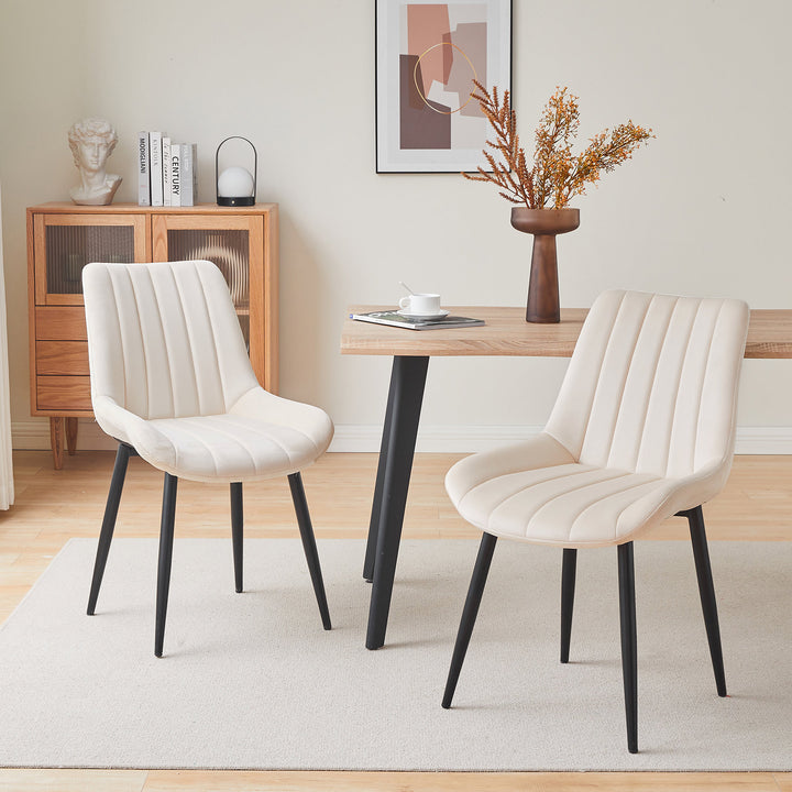 Set of 2 cream white velvet dining chairs with black metal legs, placed by a wooden dining table in a modern dining room setting