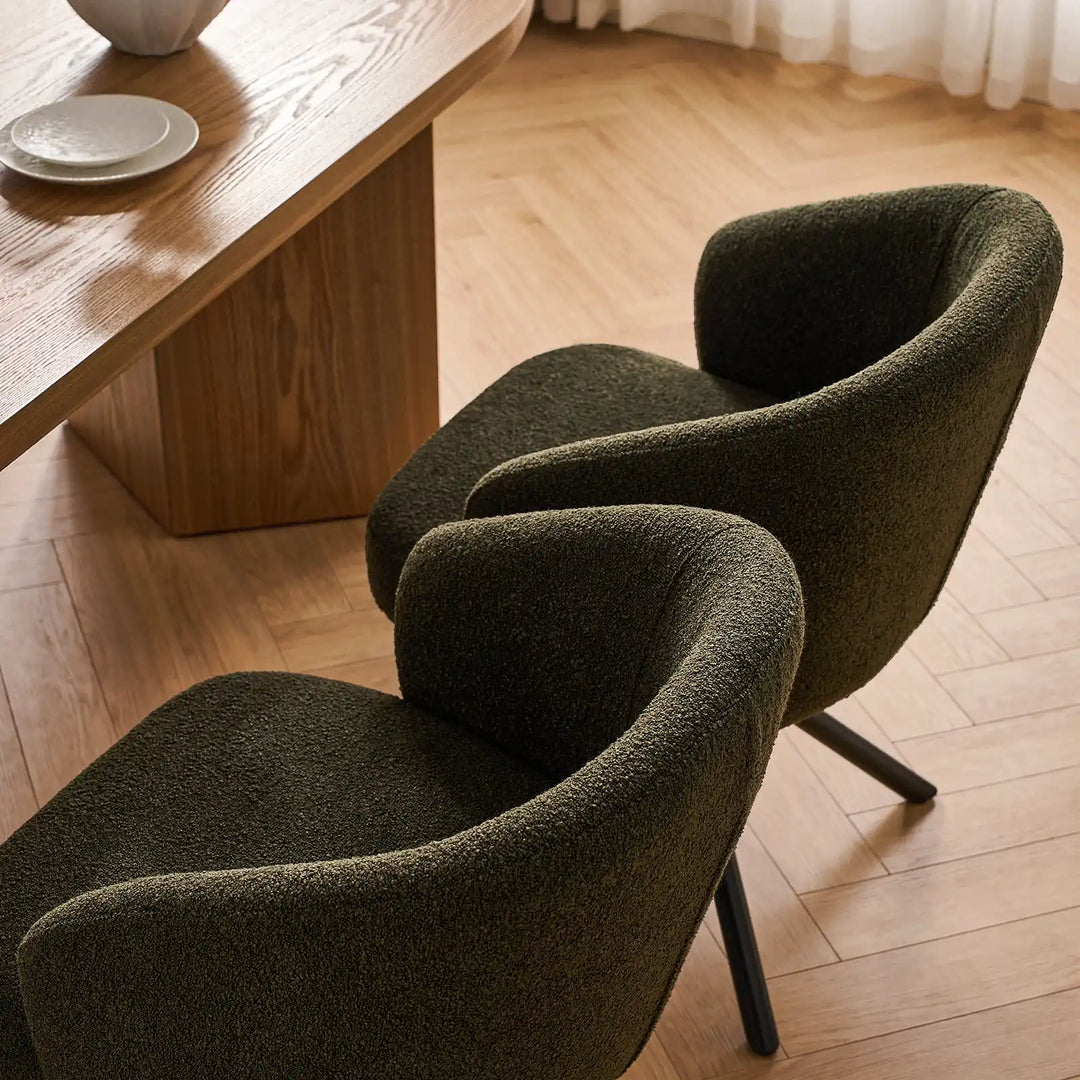 Pair of Cleo olive green bouclé swivel dining chairs arranged neatly around a wooden dining table, highlighting the rich textured fabric and curved back silhouette.