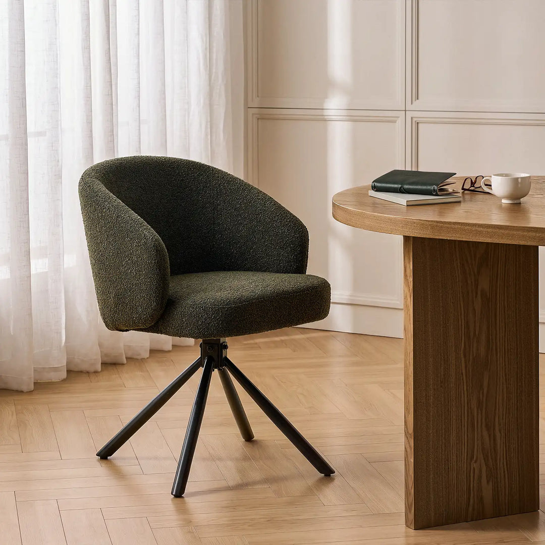 Cleo green bouclé swivel dining chair with an ergonomic tub backrest and black spider metal legs, styled beside a natural oak dining table on herringbone wood flooring in a bright modern UK home.
