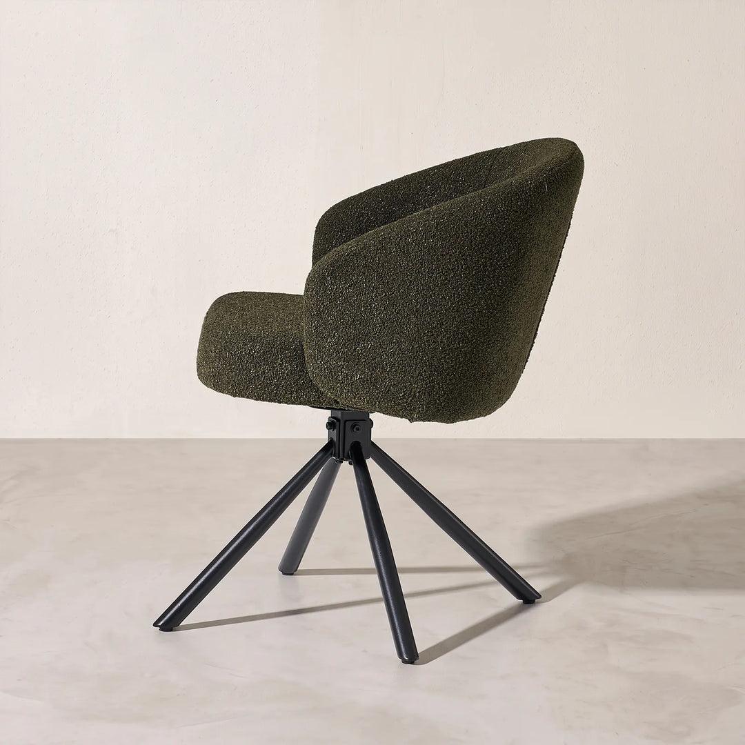 Side profile view of the Cleo green bouclé swivel armchair, displaying the smooth wrap-around tub backrest and powder-coated black metal legs.