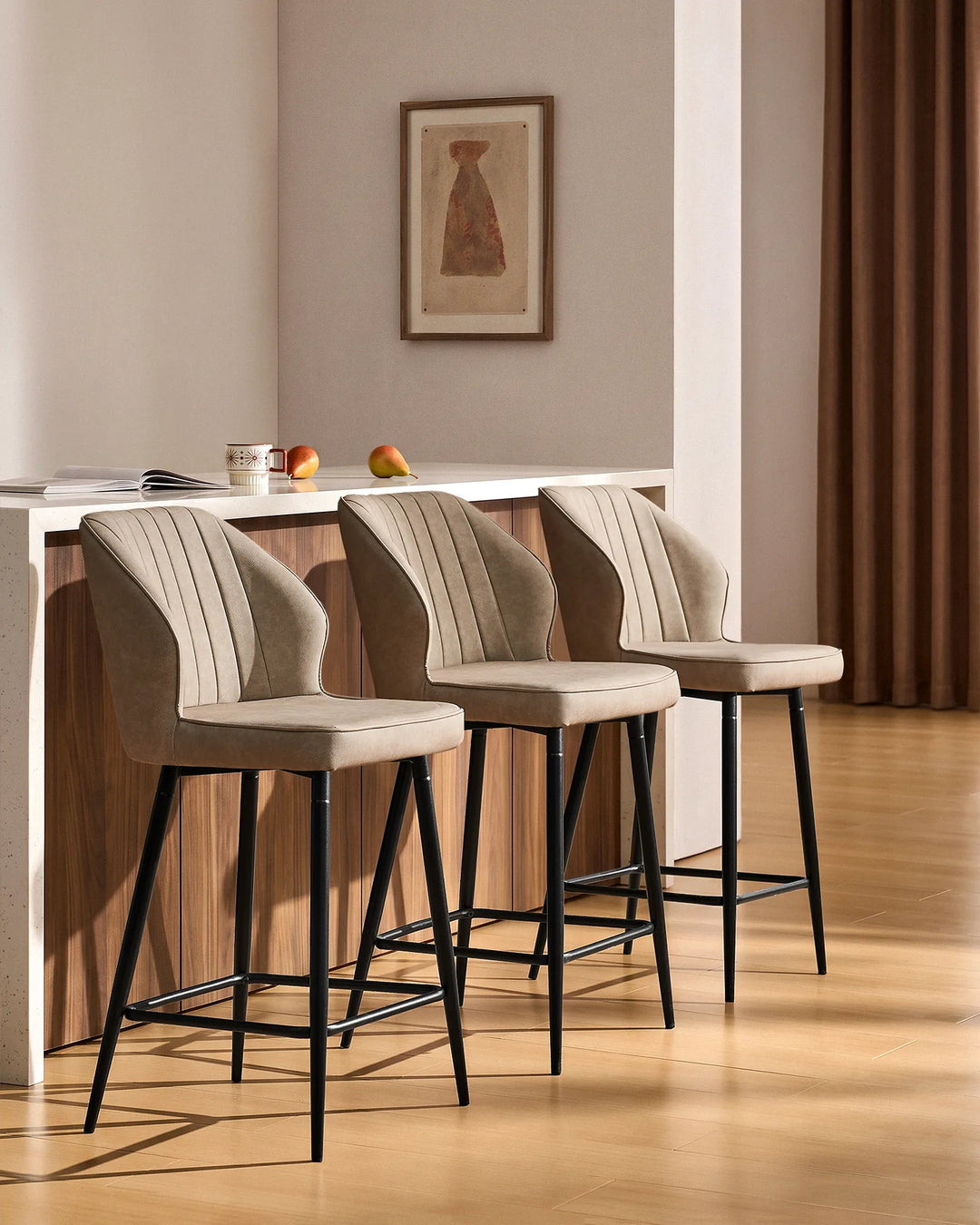 Three Danforth beige bar stools arranged along a contemporary kitchen island, featuring upholstered seats, vertical stitching and black metal frames