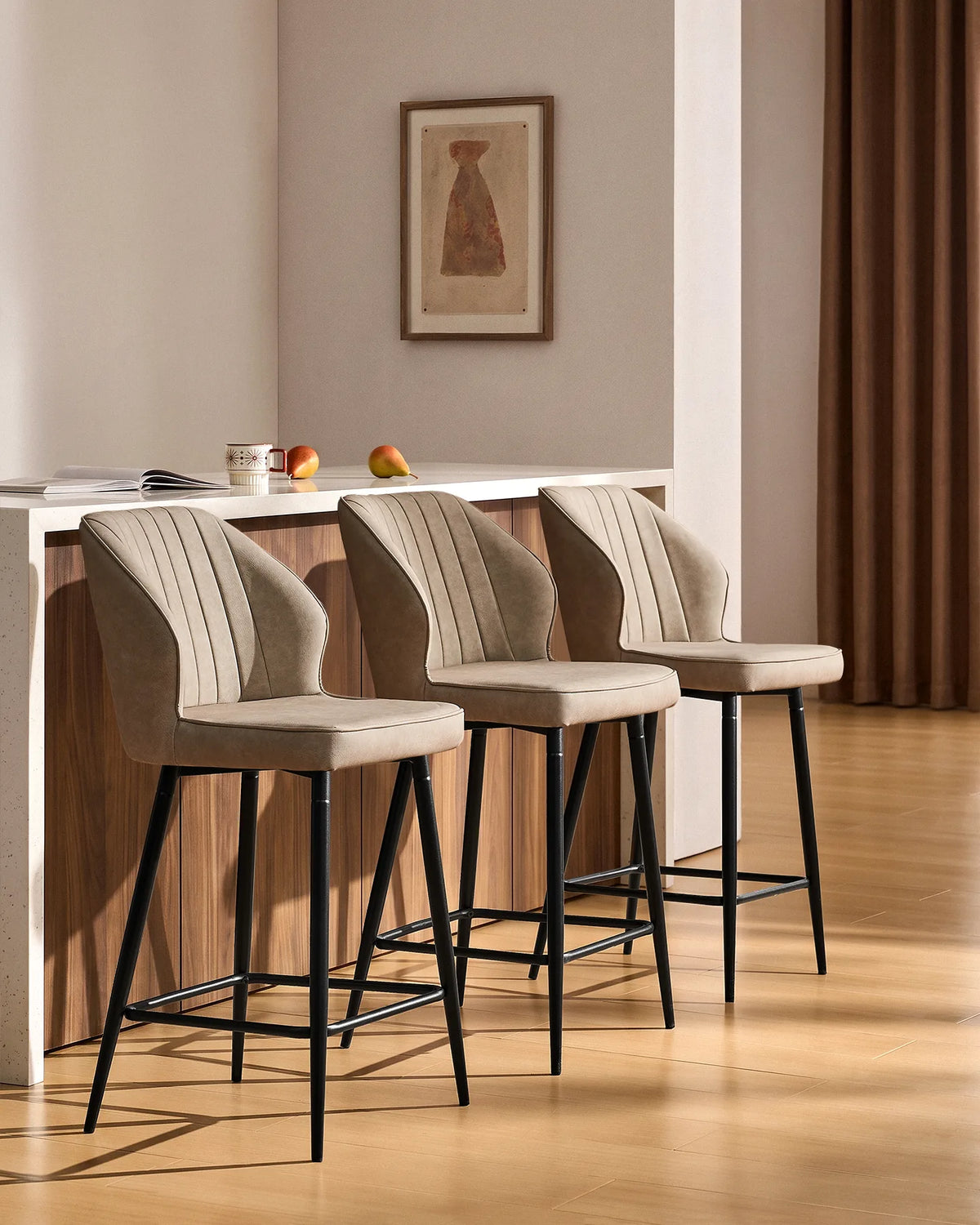 Three Danforth beige bar stools arranged along a contemporary kitchen island, featuring upholstered seats, vertical stitching and black metal frames