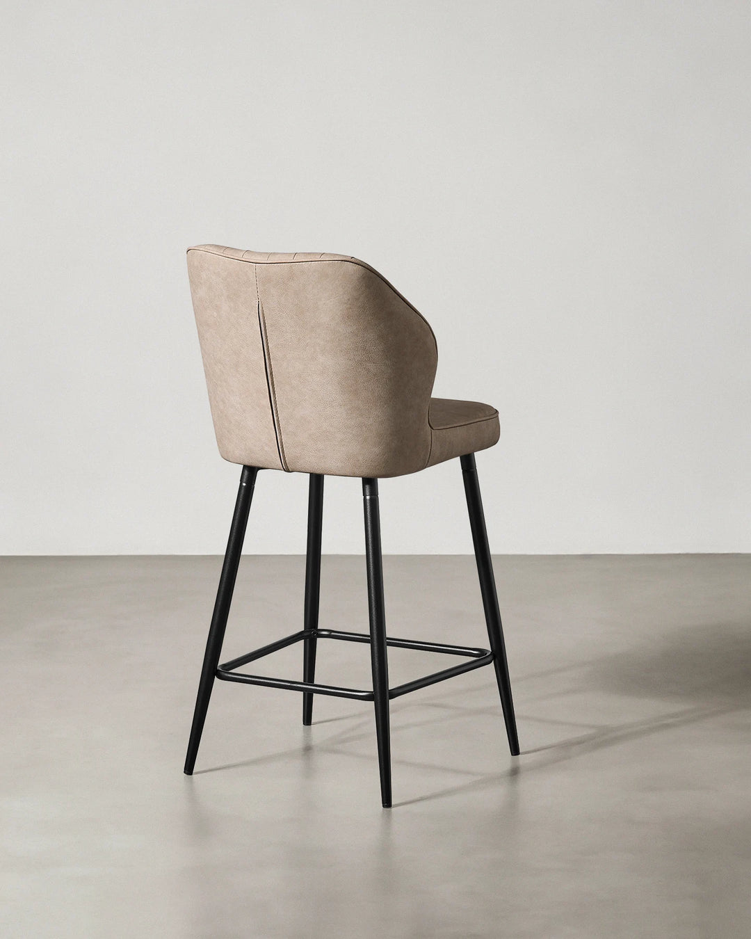 Rear view of a Danforth beige bar stool showing the upholstered backrest, curved silhouette and black metal frame