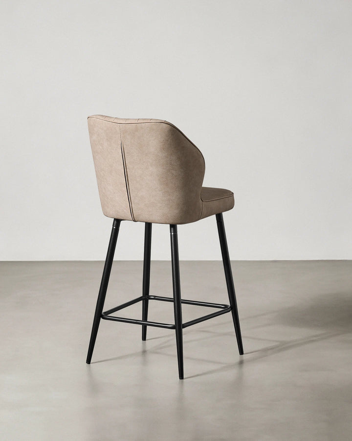 Rear view of a Danforth beige bar stool showing the upholstered backrest, curved silhouette and black metal frame