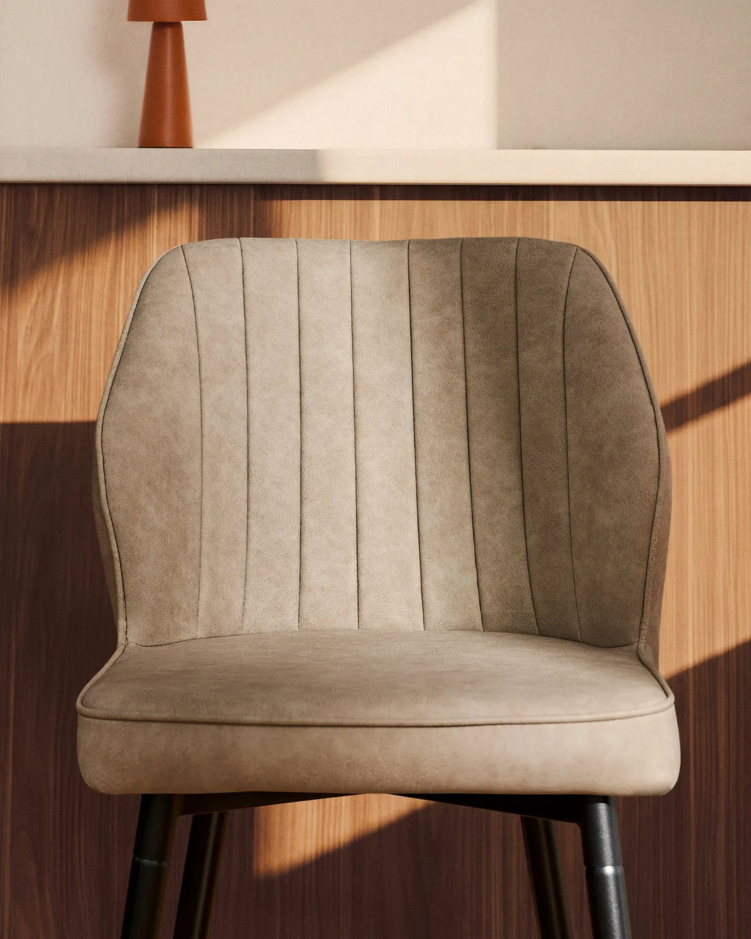 Close-up of a Danforth beige bar stool showing its softly curved backrest, padded seat, vertical channel stitching and black metal legs